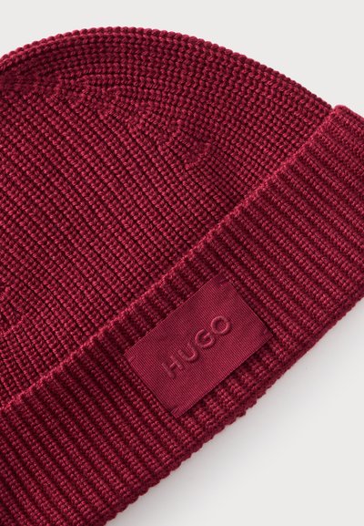 Gros plan d'un bonnet en tricot côtelé bordeaux avec un revers plié et un patch logo HUGO assorti.
