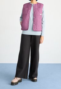 Ett kviltat lila väst med två framfickor, bärs över en ljusblå långärmad skjorta. Matchas med svarta vida byxor och platåskor.