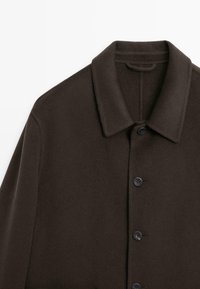 Cappotto in lana marrone con collo a camicia, lunghezza completa davanti e sei bottoni neri. Tessuto liscio con una vestibilità sartoriale.