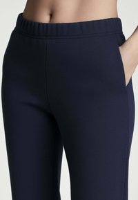 Pantaloni navy con elastico in vita, dotati di tasche laterali, texture liscia, vestibilità su misura e design minimalista. Nessun motivo o hardware visibile.