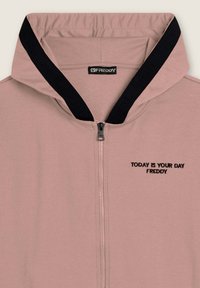 Felpa con zip di colore rosa chiaro e colletto con bordino nero, con testo ricamato "OGGI È IL TUO GIORNO FREDDY" sul petto vicino alla zip.