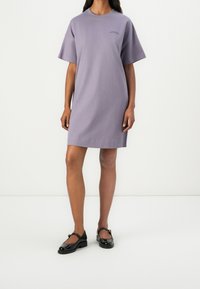 Fialové šaty s krátkým rukávem z jemné látky, s kulatým výstřihem a mírně áčkovým střihem. Nosené s černými lakovanými koženými botami.