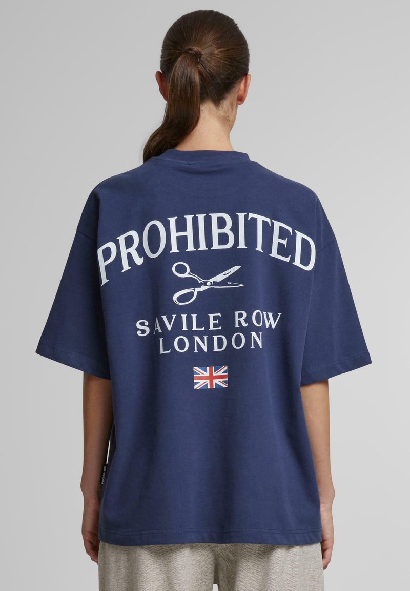 Mørkeblå oversized t-shirt med hvid "FORBUDT" tekst, saks grafik og "SAVILE ROW LONDON" nedenfor; har et britisk flag som accent.