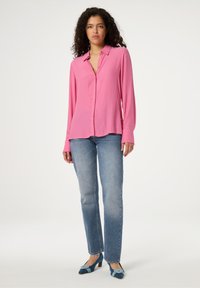 Rood langarm shirt met een kraag met knopen, gemaakt van een gladde stof; gedragen met lichtblauwe rechte jeans en bicolor hakken.