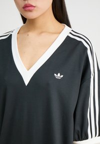 Melna lielizmēra T-kreklu ar baltu V-veida kaklu un trim baltām svītrām uz piedurknēm. Uz krūtīm ir neliels balts logo. Izgatavots no kokvilnas materiāla.
