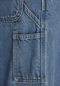 Tessuto di denim blu chiaro con texture visibile, caratterizzato da una grande tasca con cuciture gialle a contrasto lungo i bordi.