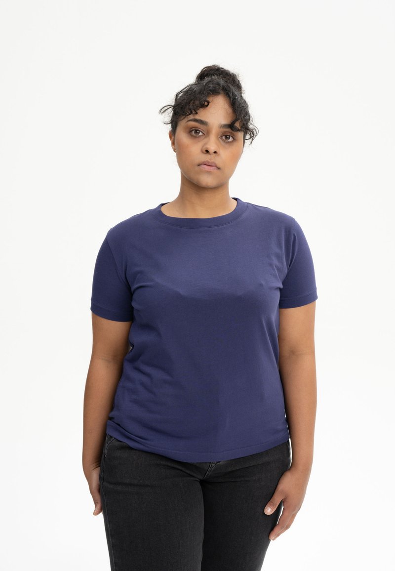 Marineblaues T-Shirt mit kurzen Ärmeln aus Baumwolle, runder Halsauschnitt, glatte Textur, getragen mit schwarzen Jeans.