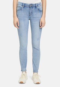 Jean skinny bleu clair en denim, avec taille mi-haute, cinq poches et légères accents de décoloration. Associé à des baskets blanches.