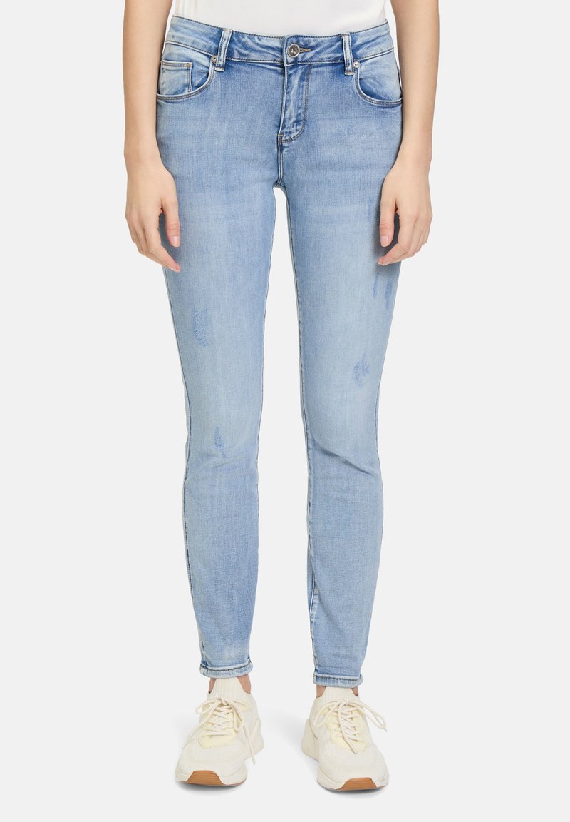 Jean skinny bleu clair en denim, avec taille mi-haute, cinq poches et légères accents de décoloration. Associé à des baskets blanches.