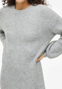 Hellgrauer gestrickter Pullover mit gerippter Textur, Rundhalsausschnitt und lockerer Passform. Mit überschnittenen Schultern und langen, leicht ausladenden Ärmeln.