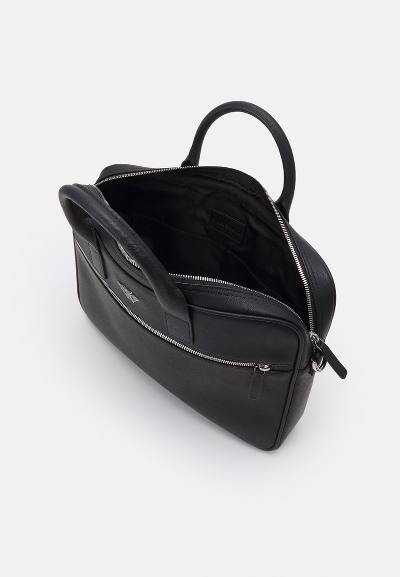 Malette en cuir noir avec fermeture éclair, poignées supérieures, une poche intérieure et une texture lisse. Dotée d'un design rectangulaire épuré.