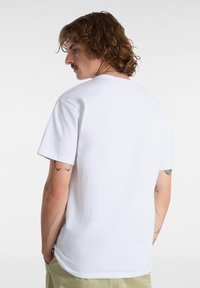 Witte katoenen t-shirt met een ronde hals en korte mouwen, gezien vanaf de achterkant. Bevat zichtbare tatoeages op de linkerarm.