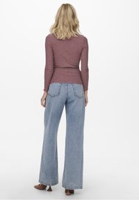 Top a maniche lunghe in maglia di colore malva, abbinato a jeans azzurri chiari a vita alta, larghi, con tasche posteriori e orlo sfilacciato.