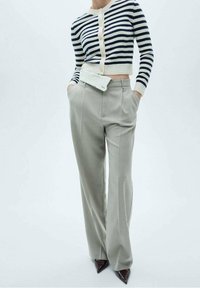 Striped cropped cardigan in cream and navy, paired with light grey high-waisted trousers. Features deep pockets, smooth fabric, and pointed heels.