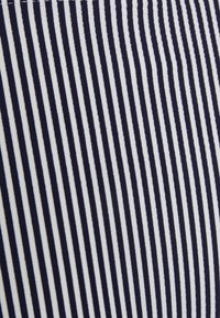 Tecido de algodão com riscas verticais em azul-marinho e branco. As riscas variam em largura, criando uma aparência texturizada.