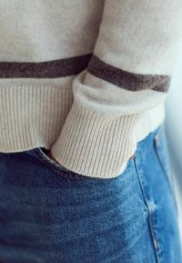 Light gray sweater with dark gray stripes, ribbed cuffs, worn over blue denim jeans. Focus on texture and material details.