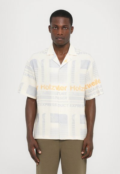 Chemise à manches courtes, à boutons, en tissu crème clair avec des motifs textuels bleus et oranges. Le col et la coupe ample augmentent le confort.