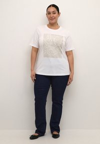 Witte katoenen t-shirt met een bloemenprint in beige, korte mouwen, gecombineerd met donkerblauwe jeans en zwarte ballerina's. Eenvoudig, casual ontwerp.