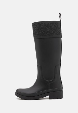 Musta kumisaapas, jossa on kuvioitu musta yläpanta, sileä pinta, hieman kaareva muoto ja matala, teksturoitu pohja.