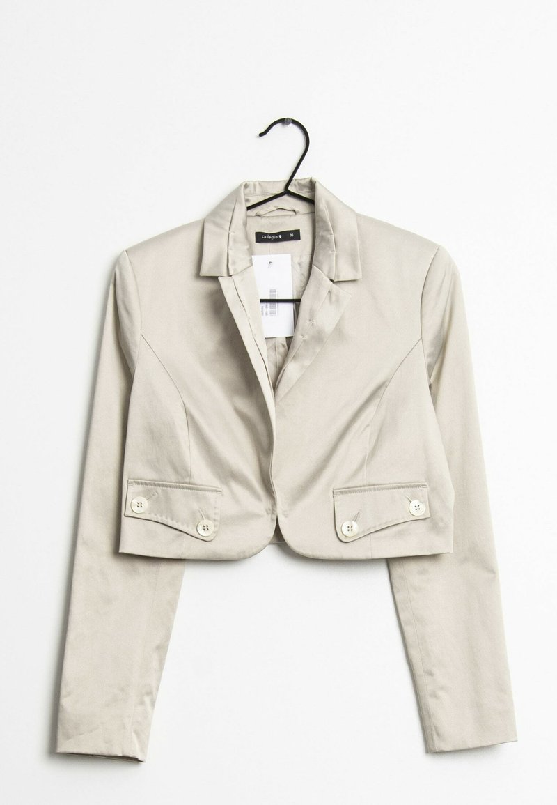 Kort beige kavaj på en galge, med en mjuk textur, skurna slag och två knappar på varje framficka.