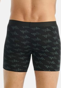 Svarta simbyxor med ett geometriskt grått mönster, tillverkade av ett glatt, stretchigt tyg, med resårmidja.