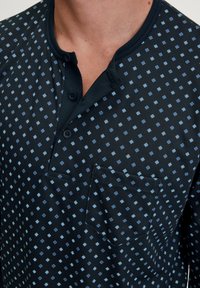 Kurzarmhemd in Marineblau mit hellblauen und dunkelblauen Quadratmustern. Verfügt über einen Kragen mit Knöpfen und eine Brusttasche mit detailliertem Stichmuster.