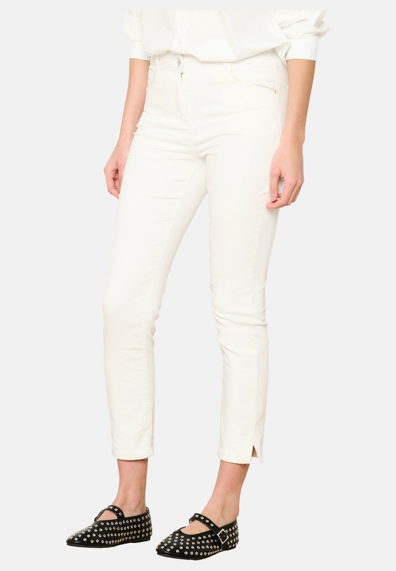 Jeans blancos ajustados con una textura suave, que presentan un diseño clásico de cinco bolsillos y dobladillos abiertos. Combinados con bailarinas negras con tachuelas.