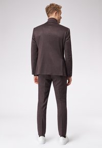 Ciemnofioletowy garnitur o dopasowanym kroju, z wysokim kołnierzem i eleganckimi liniami. Połączony z białymi trampkami, co nadaje nowoczesny akcent.