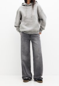 Grijze hoodie met capuchon en een voorzak, gecombineerd met loszittende, vervaagde grijze jeans en zwarte sneakers met lichtbruine zolen.