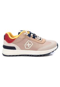 Zapato deportivo beige con parte superior texturizada, cordones azul marino y acentos rojos. Presenta una suela blanca gruesa y un emblema del logo en el lateral.
