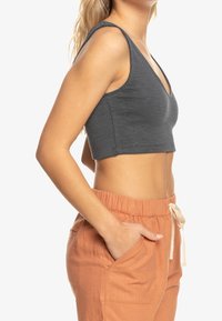 Grå, ribbet crop top med V-udskæring, tynde stropper og tætsiddende design, parret med lyseorange trækstringbukser med sidelommer.