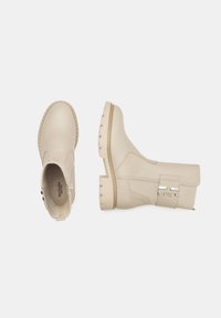 Bottes ankle beiges en cuir lisse, avec une semelle épaisse, une fermeture éclair latérale et des accents métalliques pour la fermeture.