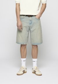 Pantalones cortos de mezclilla azul claro con un ajuste relajado, dobladillo deshilachado y diseño clásico de cinco bolsillos. Combinados con calcetines blancos y zapatillas beige.
