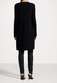 Svart långärmad stickad klänning med rak skärning, rund halsringning och texturerat tyg. Kombinerad med svarta skinny byxor och klackskor.