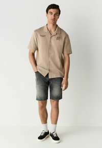Short-sleeved beige shirt with button front, embroidered detail, paired with gray denim shorts and black sneakers with white laces.