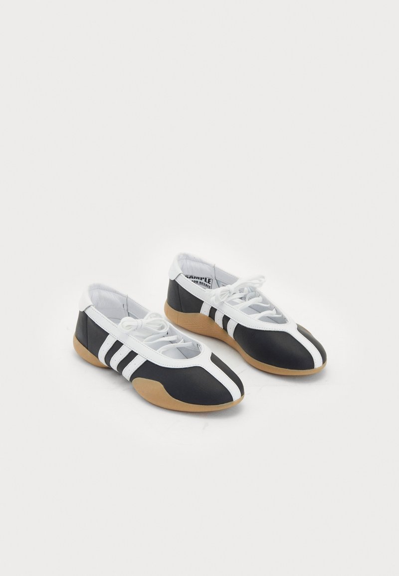 Black and white athletic shoes with a sleek design, rubber sole, lace-up closure, and three white stripes on the sides.
