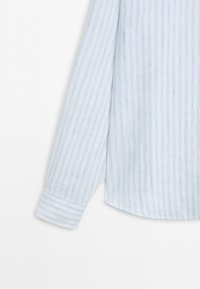 Light blue long sleeve shirt with thin vertical white and darker blue stripes, shown from the back against a white background.