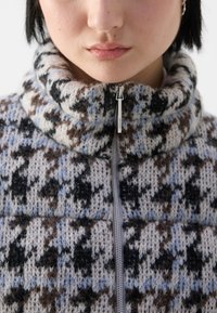Strickpullover mit hohem Kragen, der eine gemusterte Textur in Brauntönen, Schwarz und Blautönen aufweist, mit einem silbernen Reißverschlussdetail.