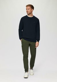 Navy-blaues Strick-Sweatshirt mit geripptem Kragen, kombiniert mit olivgrünen Cargo-Hosen mit Seitentaschen. Weiße Sneaker runden das Outfit ab.