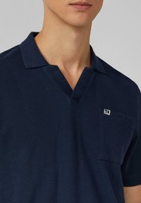 Marineblauwe polo met een textuurstof, een V-halslijn en een borstzak met een klein logo. Korte mouwen en een gestructureerde pasvorm.