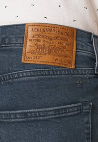 Nahkainen Levi Strauss & Co. -labeli sinisissä farkuissa, joissa on koko W31 L32 ja Lot 512, tikattu takataskun yläpuolelle.