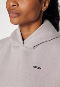 Šviesiai pilka džemperis su plačiu apykaklės kraštu, pagamintas iš minkštos medžiagos, su mažuoju juodu "Under Armour" logotipu. Lygi tekstūra, paprastas dizainas.