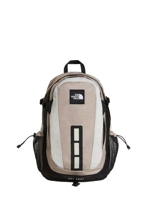 Beżowo-czarny plecak The North Face Hot Shot z siateczkowymi bocznymi kieszeniami i górnym uchwytem do przenoszenia, pokazany w pozycji pionowej.