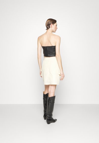 Top sans bretelles en cuir noir, jupe blanche longueur genoux avec poches latérales, et bottes noires en cuir verni jusqu'aux genoux. Textures douces et design simple.