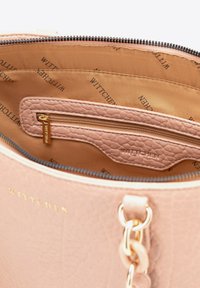 Lichtroze handtas met een gestructureerde leren buitenkant. Het interieur heeft een gladde tan voering en een ritszak. Merknnaam is in het interieur geperst.