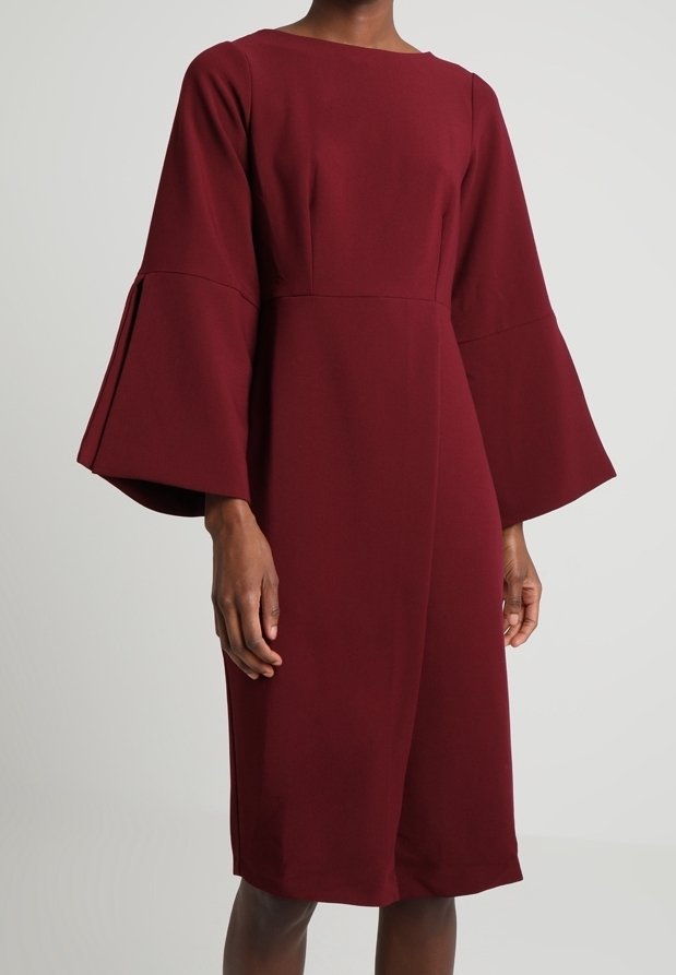 Viininpunainen mekko, jossa on neliömäinen pääntie, pitkät liehukevät hihat, jämäkkä vartaloosa ja polvipituinen helma. Valmistettu sileästä, teksturoidusta kankaasta.