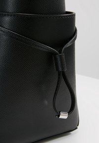 Zwart gestructureerd leren tas met een functionele trekkoordsluiting met een zilveren accent. Het ontwerp is minimalistisch en gestructureerd.