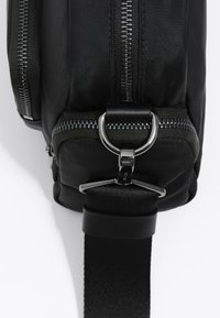 Must mustriga seljakott, millel on kaks tõmblukk, ringikujuline reklaamielement ja tekstuuriga rihm turvaliseks kandmiseks.