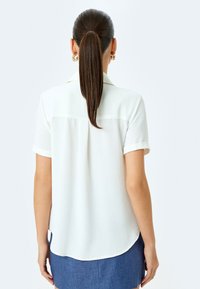 Witte shirt met korte mouwen, voorzien van een puntige kraag, opgerolde mouwen, een afgeronde zoom en een zachte stoftextuur.