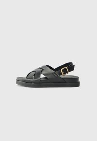 Black leather sandal with a woven strap design, flat sole, and adjustable ankle buckle, featuring a smooth surface and minimalist style.